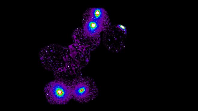 Esta imagen muestra el nuevo filamento, que conecta cuatro cúmulos de galaxias: dos en un extremo y dos en el otro. Estos cúmulos son visibles como puntos brillantes en la parte inferior y superior del filamento (cuatro puntos blancos rodeados de color). Una banda moteada de color púrpura se extiende entre estos puntos brillantes, destacando con fuerza contra el cielo negro circundante. Este es el filamento de gas caliente emisor de rayos X que no se había visto antes y que contiene un trozo de materia «perdida». La banda púrpura comprende datos de Suzaku. Los astrónomos lograron identificar y eliminar cualquier posible fuente de contaminación de rayos X del filamento utilizando XMM-Newton, dejando tras de sí un hilo puro de materia faltante. Estas fuentes se pueden ver aquí como puntos brillantes que atraviesan y se eliminan de la emisión del filamento. Crédito: ESA/XMM-Newton and ISAS/JAXA