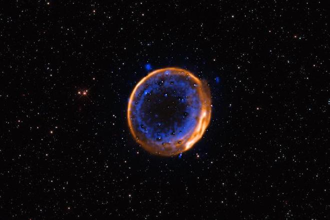 Esta imagen, tomada con el Very Large Telescope (VLT) de ESO, muestra el remanente de supernova SNR 0509-67.5. Estos son los restos en expansión de una estrella que explotó hace cientos de años en una doble detonación, la primera evidencia fotográfica de que las estrellas pueden morir con dos explosiones. Los datos se capturaron con el instrumento Multi-Unit Spectroscopic Explorer (MUSE) del VLT. MUSE permite a los astrónomos mapear la distribución de diferentes elementos químicos, que se muestran aquí en diferentes colores. El calcio se muestra en azul y está dispuesto en dos capas concéntricas. Estas dos capas indican que la estrella ahora muerta explotó con una doble detonación. Crédito: ESO/P. Das et al. Estrellas de fondo (Hubble): K. Noll et al.